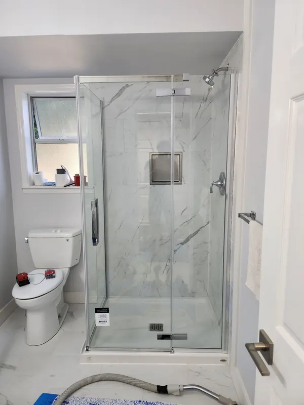 Corner glass shower with marble-look tile and a recessed niche