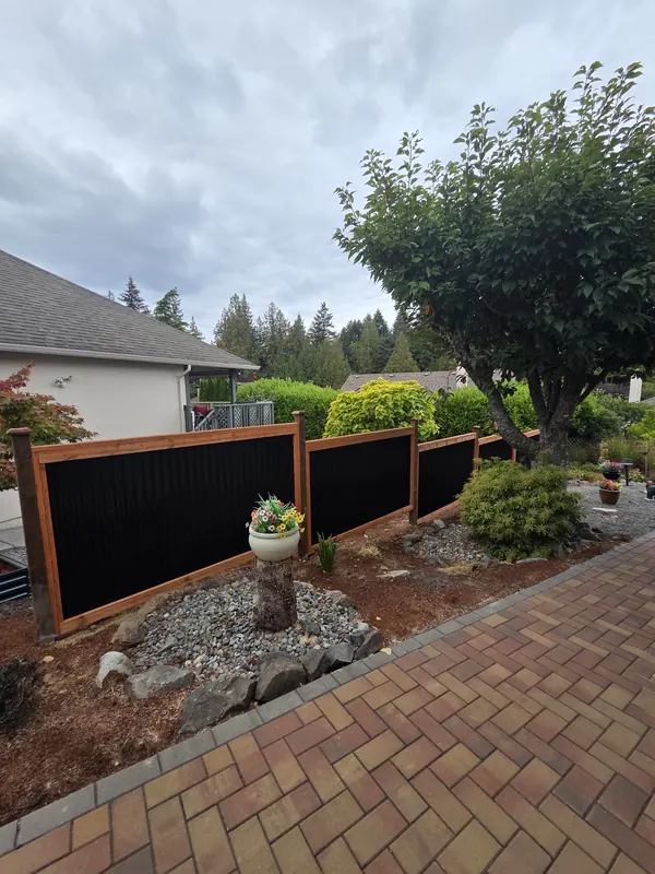 Black metal garden fence panels in cedar frames beside a paver path