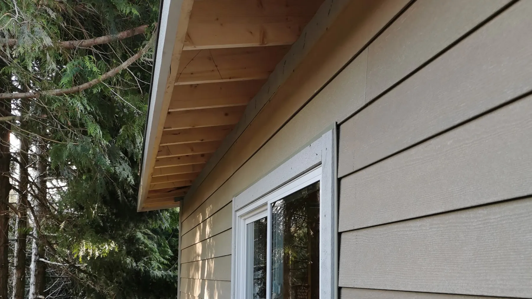 New beige lap siding and a cedar soffit on a garage wall with a white window