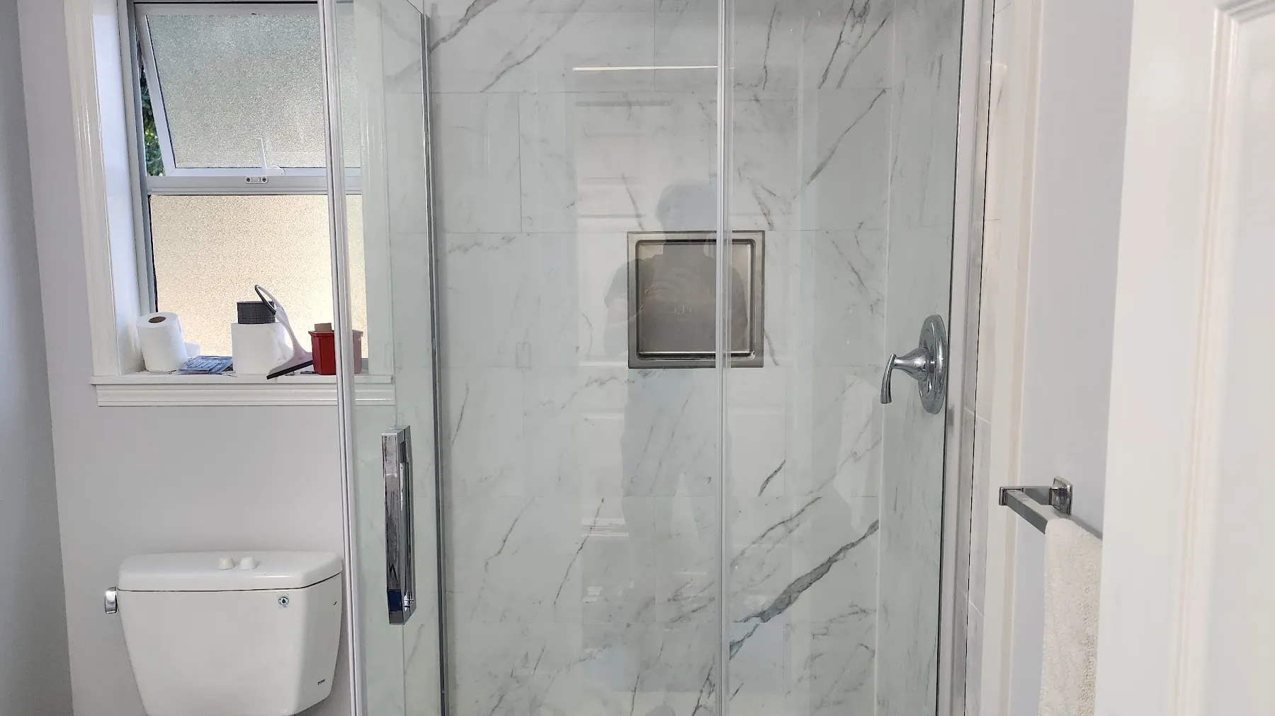 Corner glass shower with marble-look tile and a recessed niche