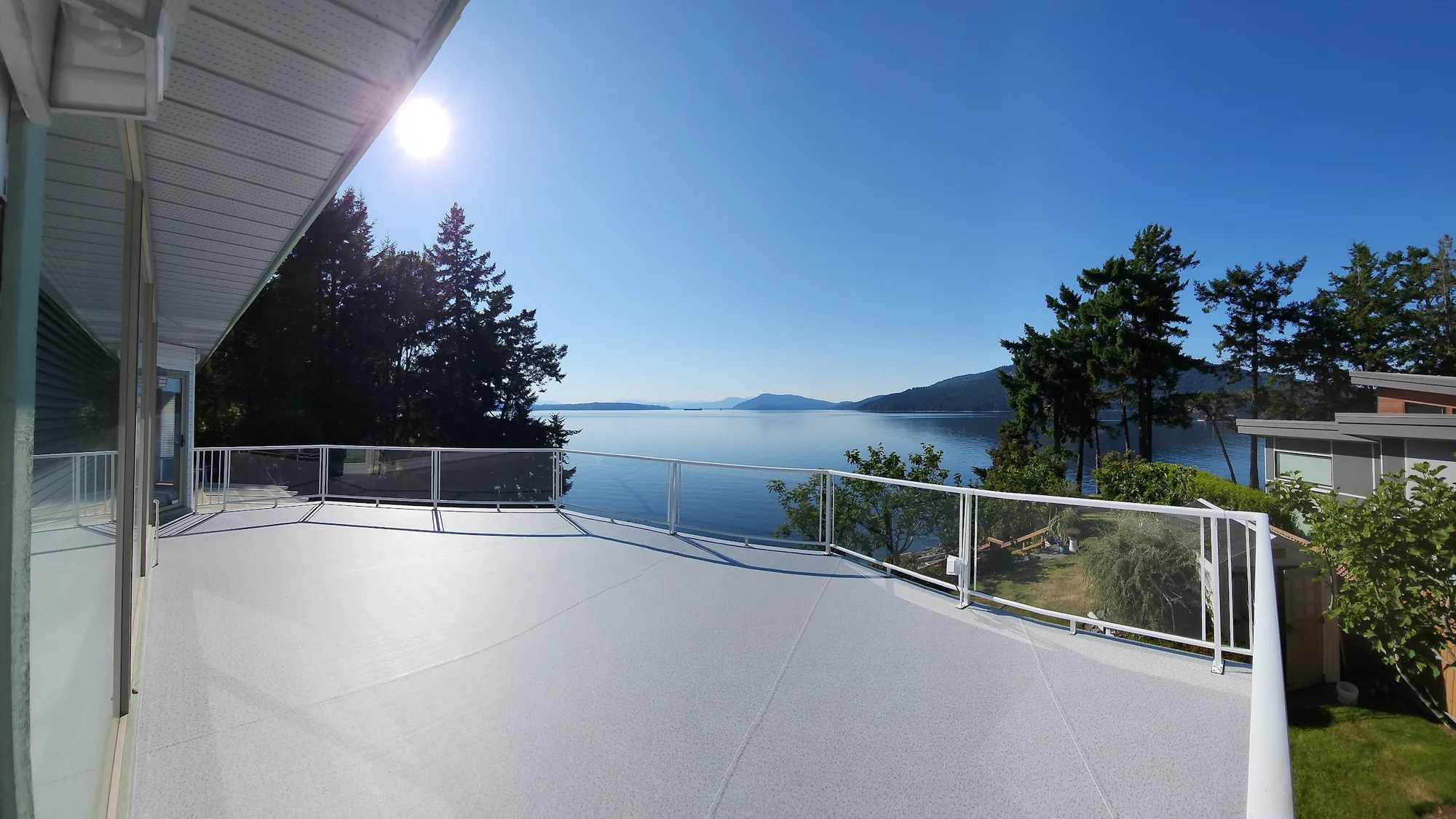 Light speckled vinyl deck with a white aluminum and glass railing, the sun over the water and islands beyond