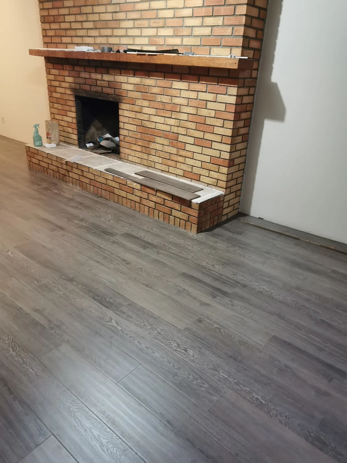 New grey plank flooring in front of a brick fireplace