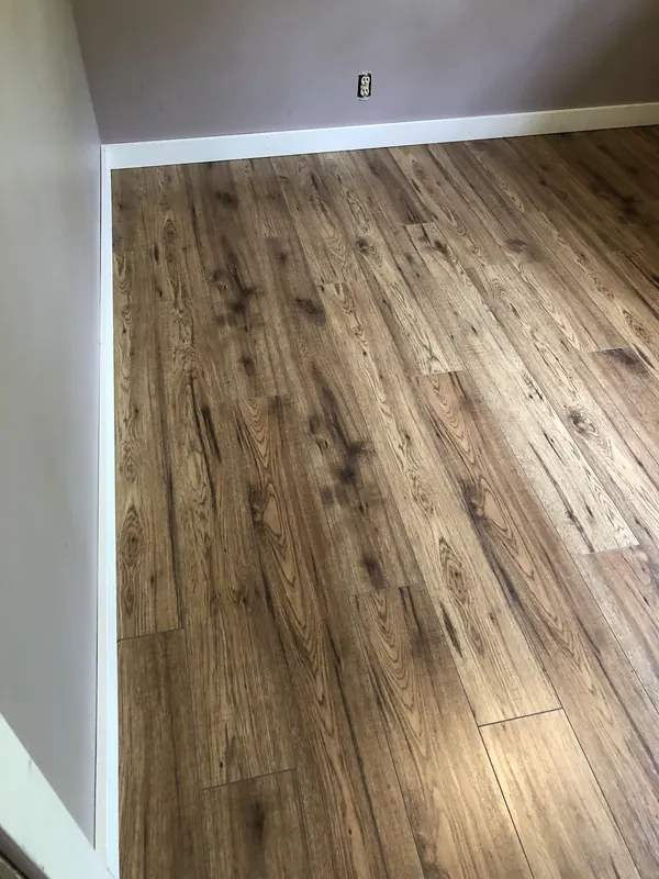 New rustic wood-look laminate flooring with white baseboard