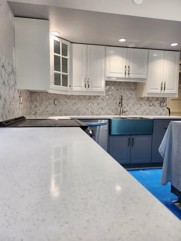 White kitchen cabinets with a herringbone backsplash and quartz counter