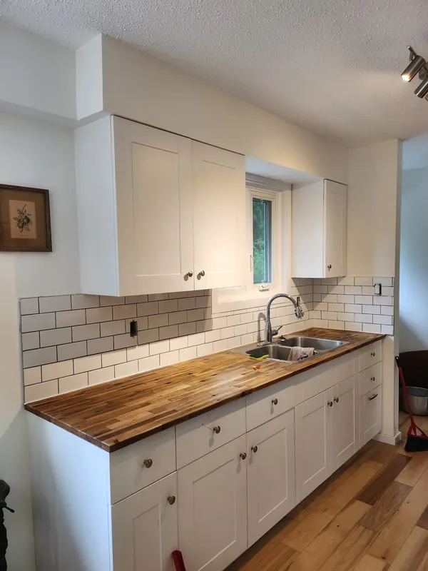 White shaker kitchen cabinets with a butcher-block counter and subway tile