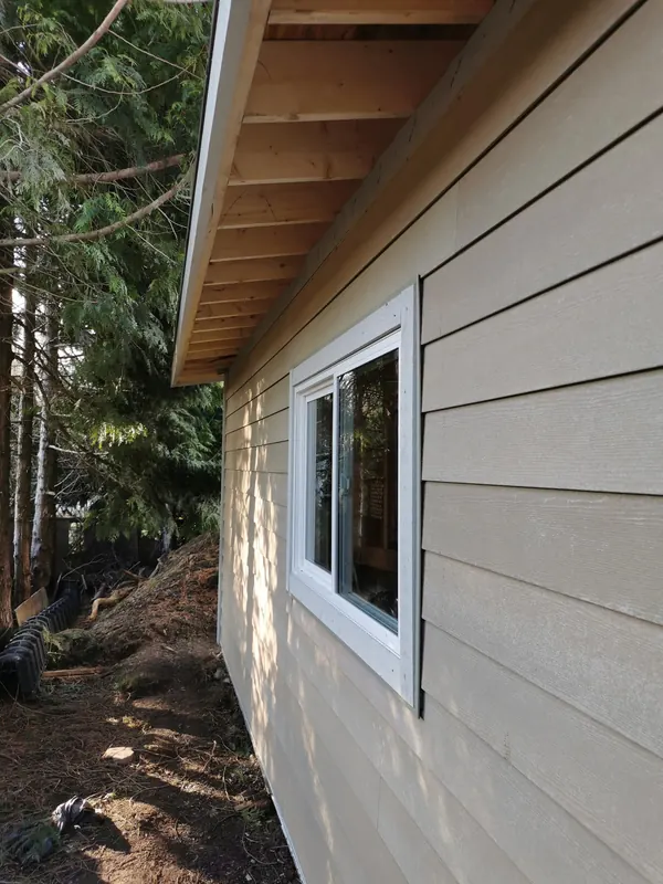 New beige lap siding and a cedar soffit on a garage wall with a white window