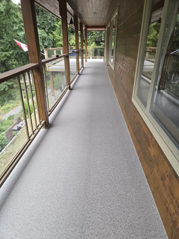 Covered vinyl walkway deck with cedar posts and glass panel railing along a cedar-clad house