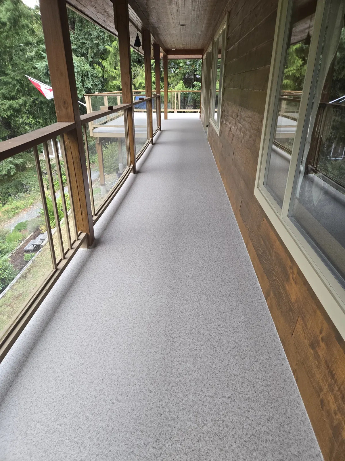Covered vinyl walkway deck with cedar posts and glass panel railing along a cedar-clad house