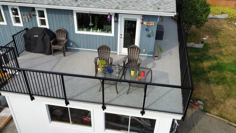 Drone view of a grey speckled vinyl deck with a black aluminum railing and patio chairs on a blue house