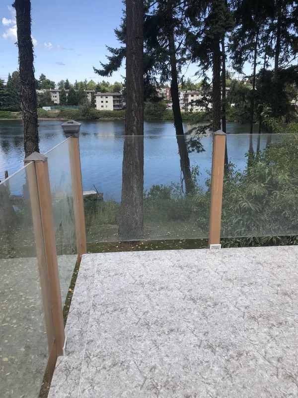 Topless glass railing on a speckled vinyl deck, the glass set between cedar posts with a lake view beyond