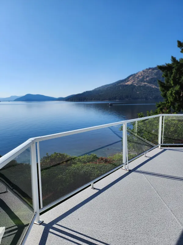 Corner of a speckled vinyl deck with a glass railing and a wide view of the sea and mountains