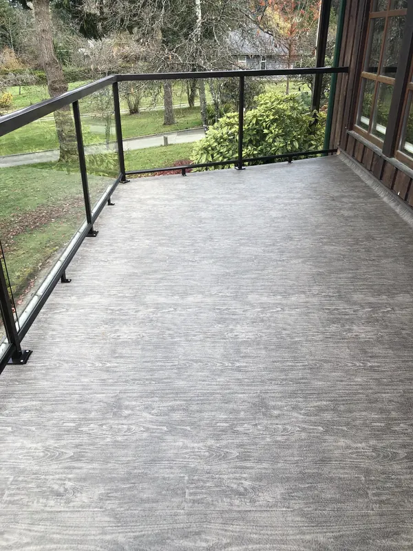 Grey wood-grain vinyl deck with a black-framed glass railing beside a cedar-clad house